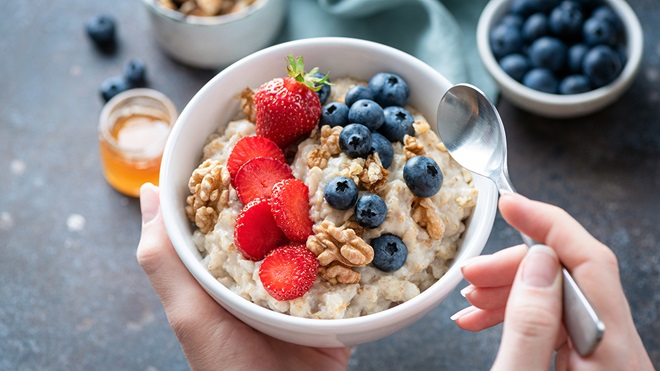 hands_holding_a_bowl_of_oatmeal_porridge_with_strawberries_blueberries_and_walnuts